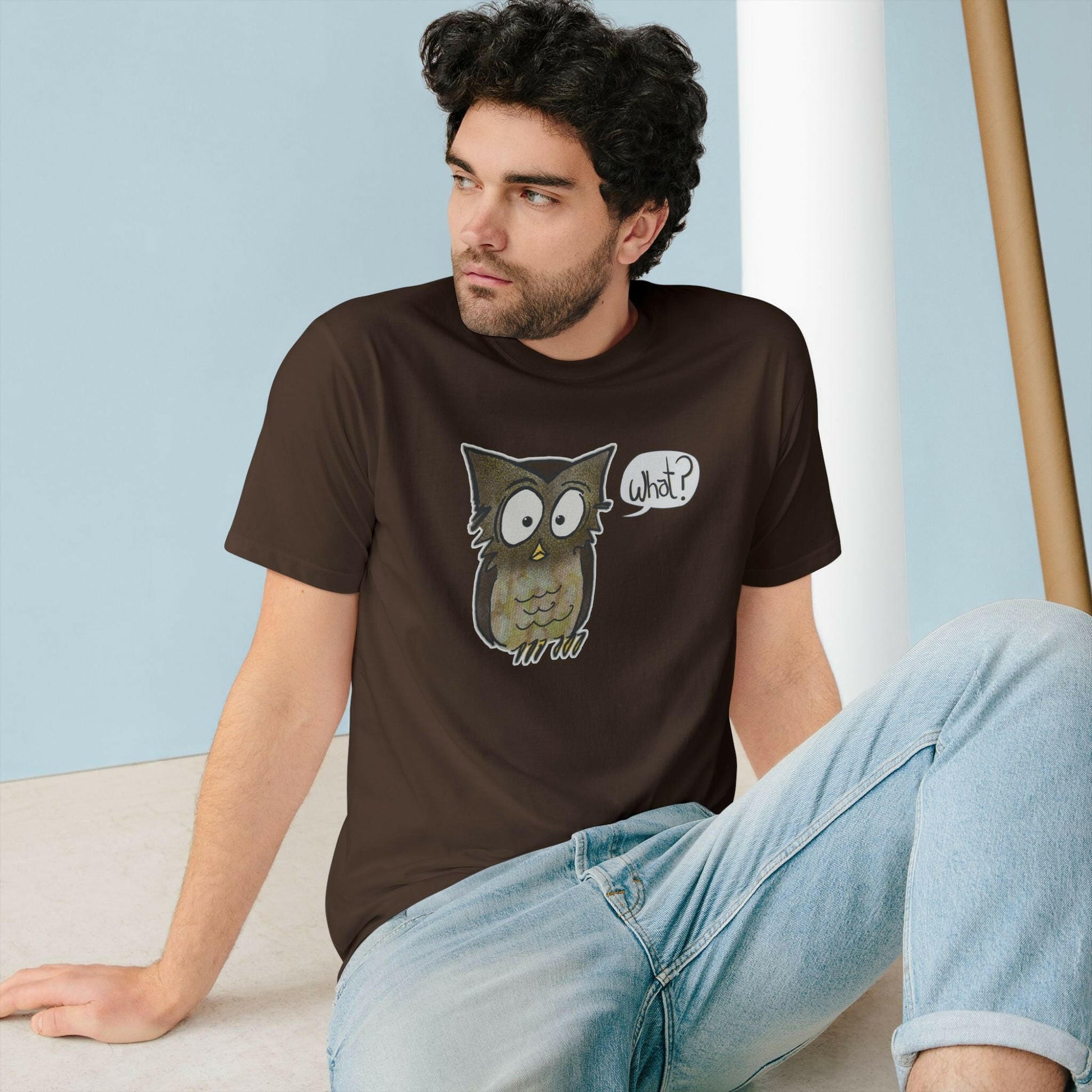 Man wearing a brown t-shirt with an owl graphic sitting on the floor.