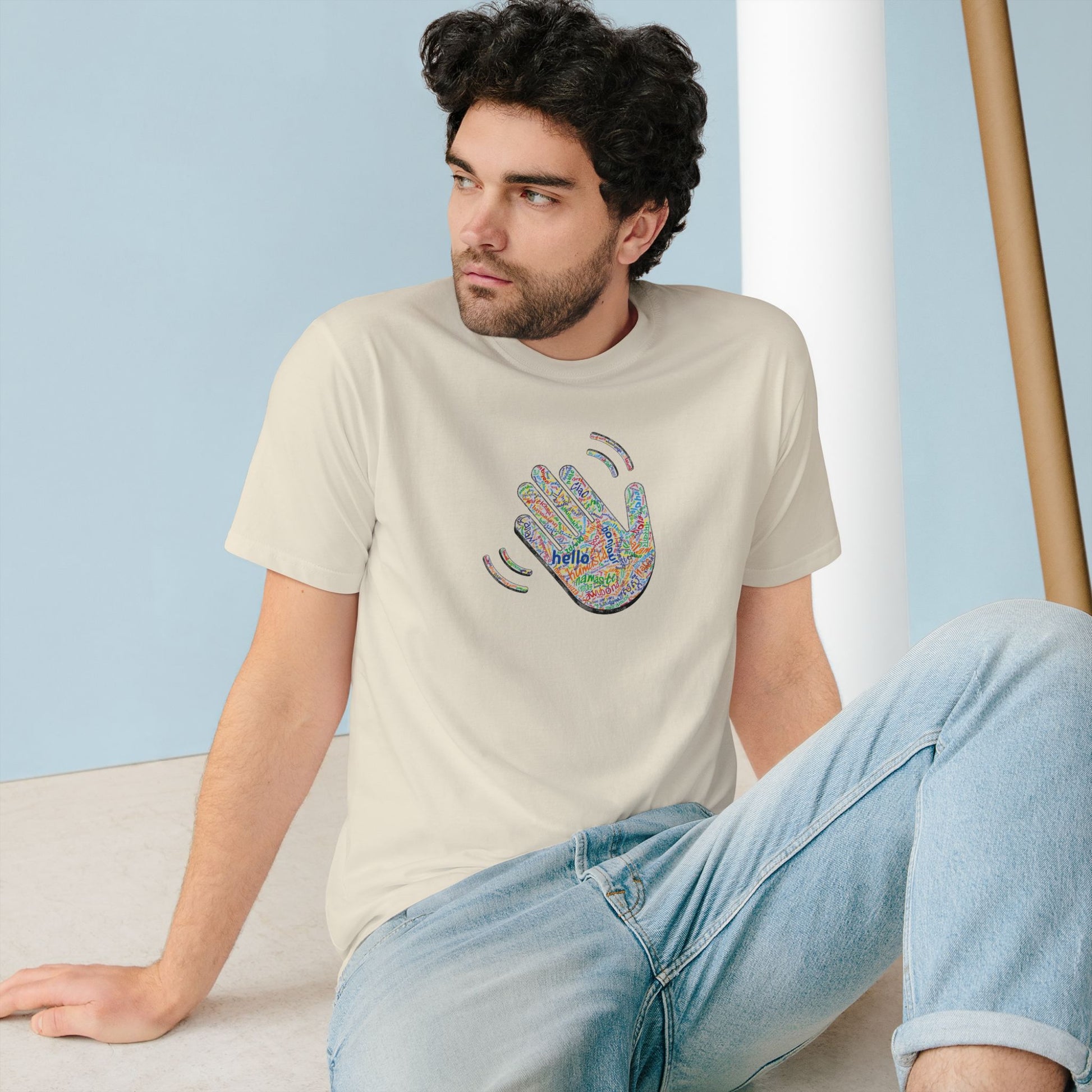 Man wearing a beige t-shirt with a colorful handprint design sitting on the floor.