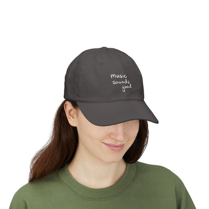 Woman wearing a dark gray cap with 'music sounds good' text on a white background