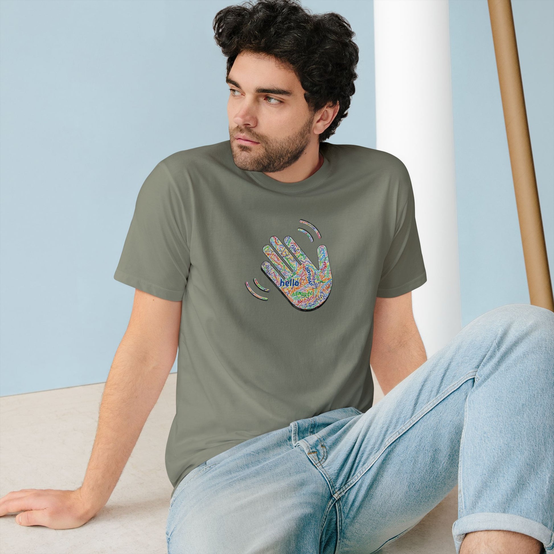 Man wearing a olive green t-shirt with a colorful handprint design sitting on the floor