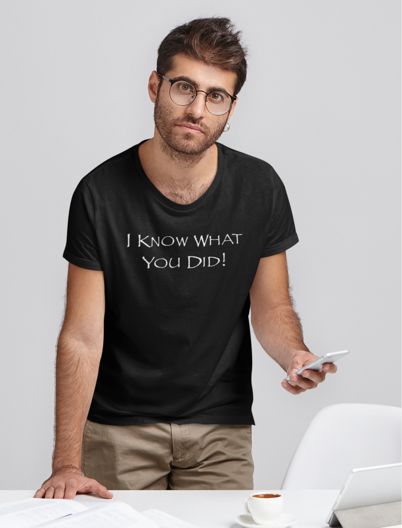 man with glasses standing at work desk wearing T-shirt that says "I Know What You Did!"
