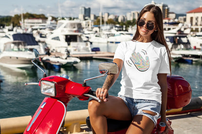 Woman sitting on a red scooter by a marina with boats and buildings in the background wearing a white Think a Thunk Hello ASL Hand Graphic Tee - Multi-Language Greeting T-Shirt.