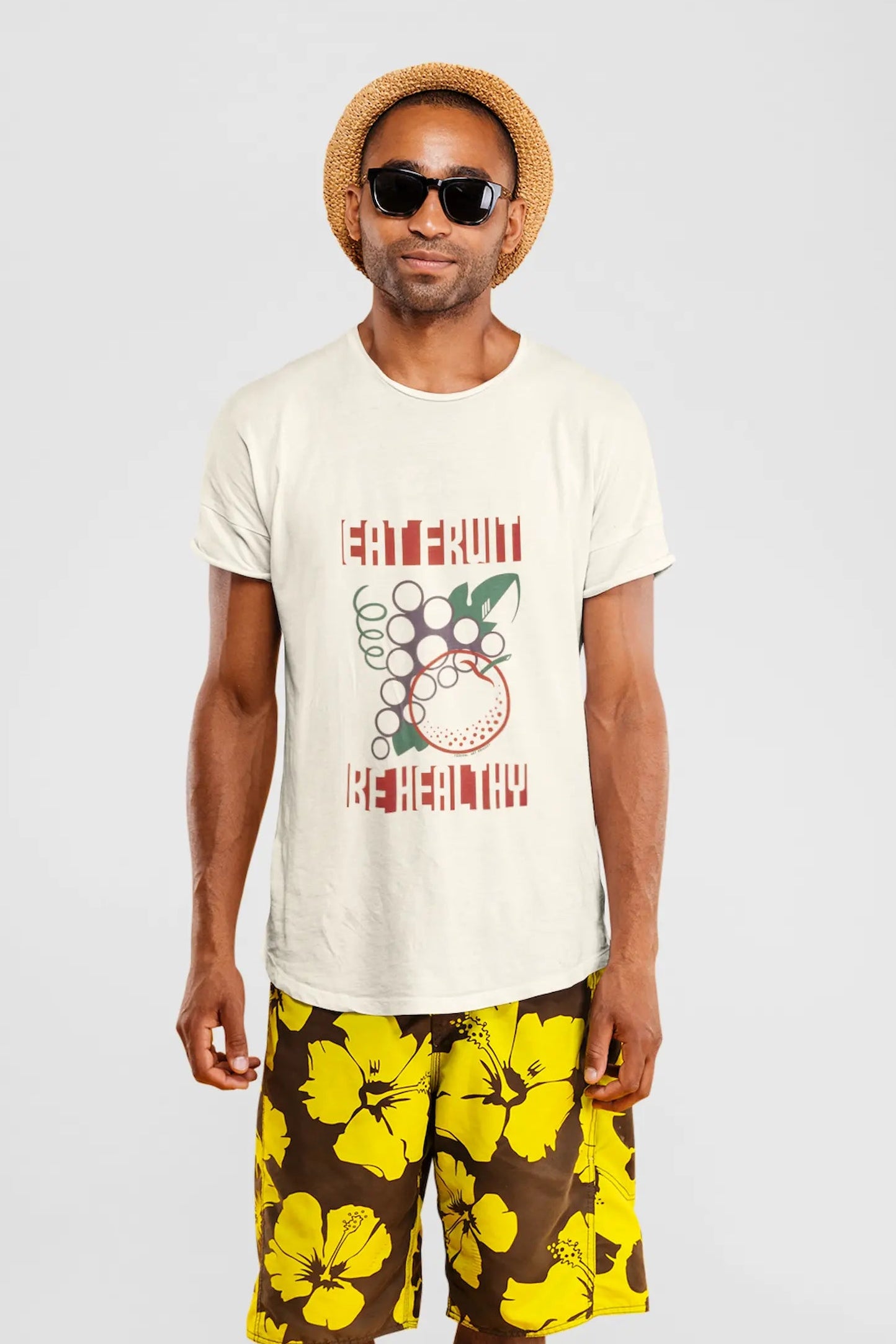 Man wearing a natural colored Think a Thunk Unisex Eat Fruit Be Healthy T-Shirt and floral shorts on a white background