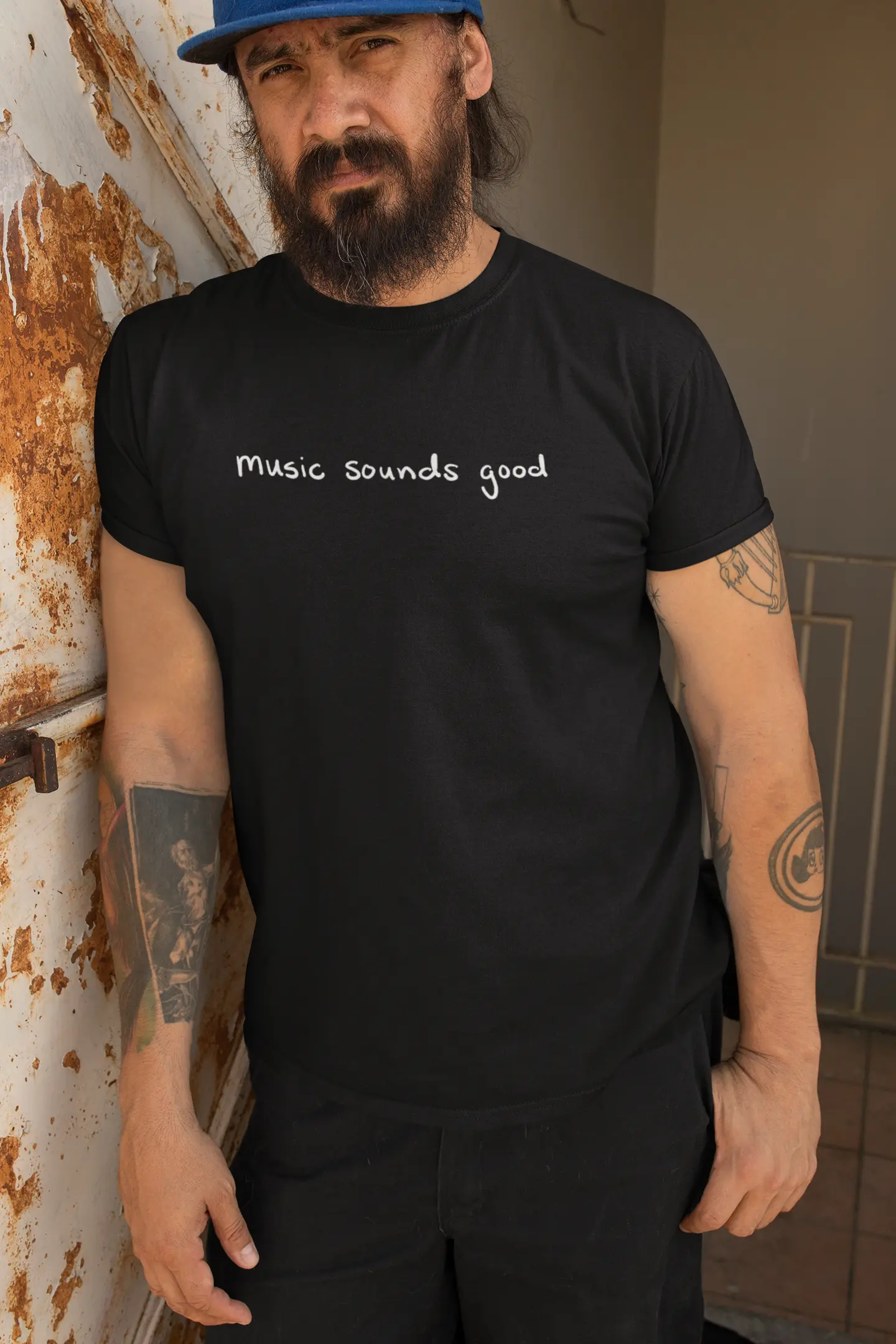 Man wearing a black Think a Thunk Unisex Music Sounds Good T-Shirt, leaning against a wall.