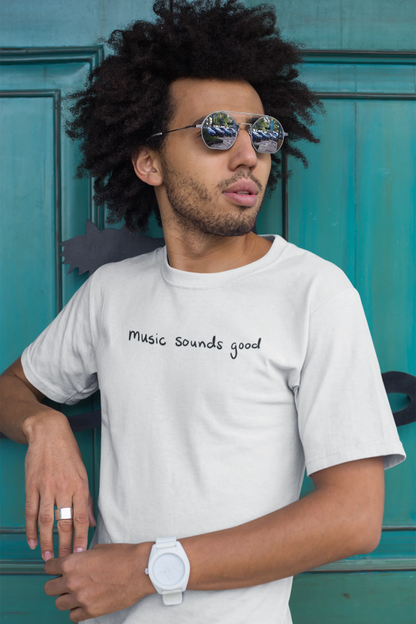 Man wearing a white Think a Thunk Unisex Music Sounds Good T-Shirt , sunglasses, and a watch against a teal door.