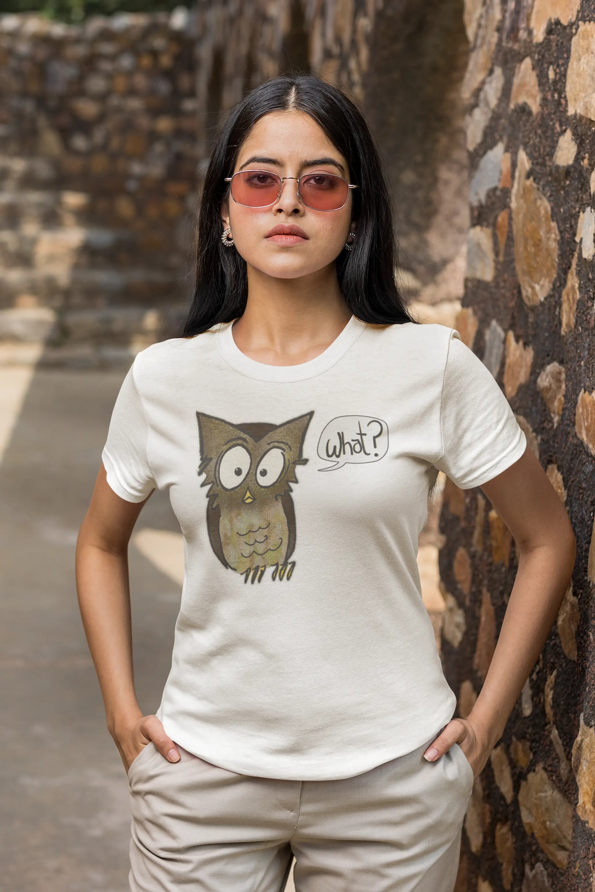 Woman wearing a white Think a Thunk Unisex Perplexed Owl Organic T-Shirt, standing against a stone wall.