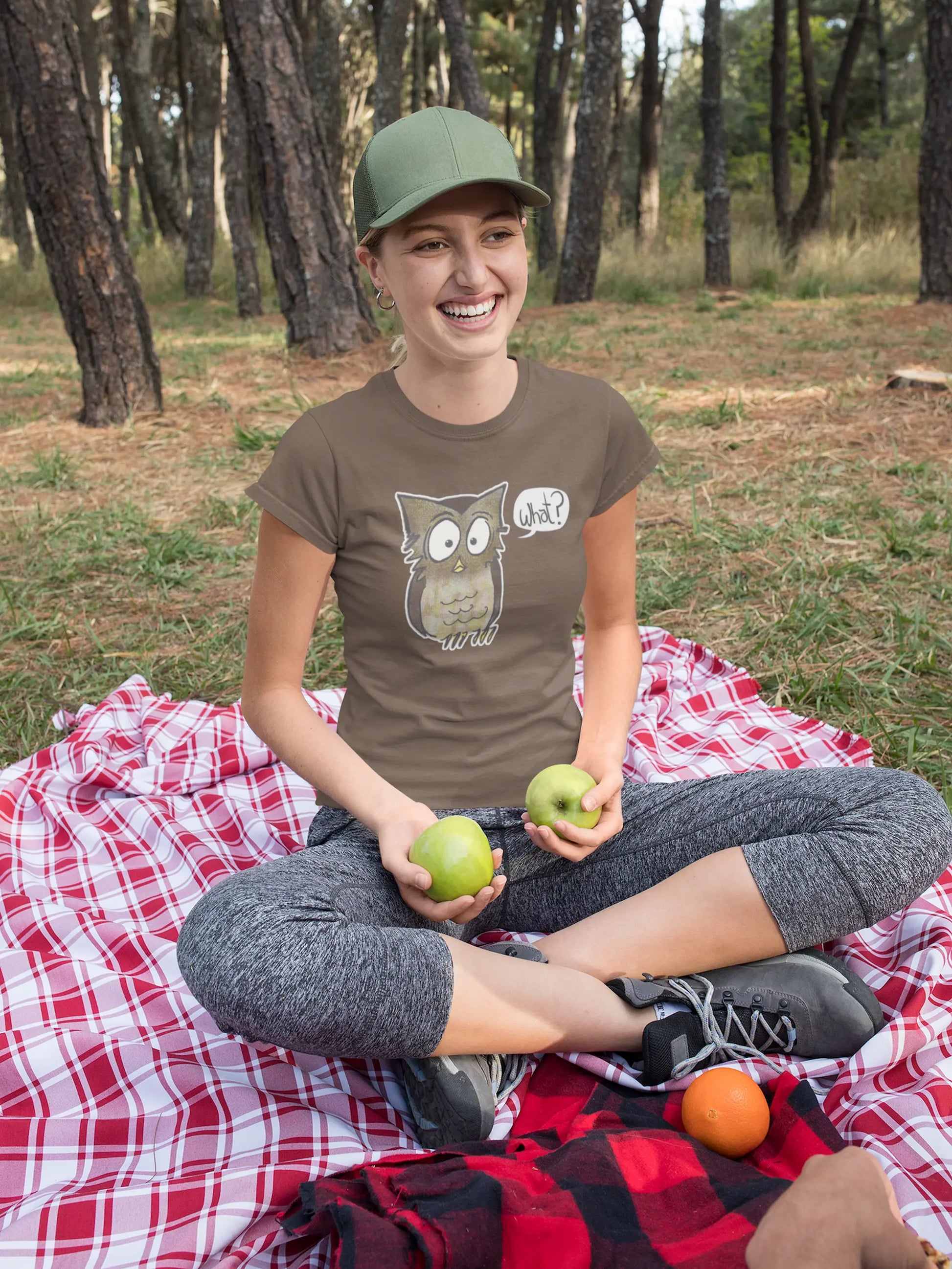 Woman sitting on a red and white checkered blanket in a forest, holding apples - wearing a walnut colored Think a Thunk Unisex Perplexed Owl Organic T-Shirt 
