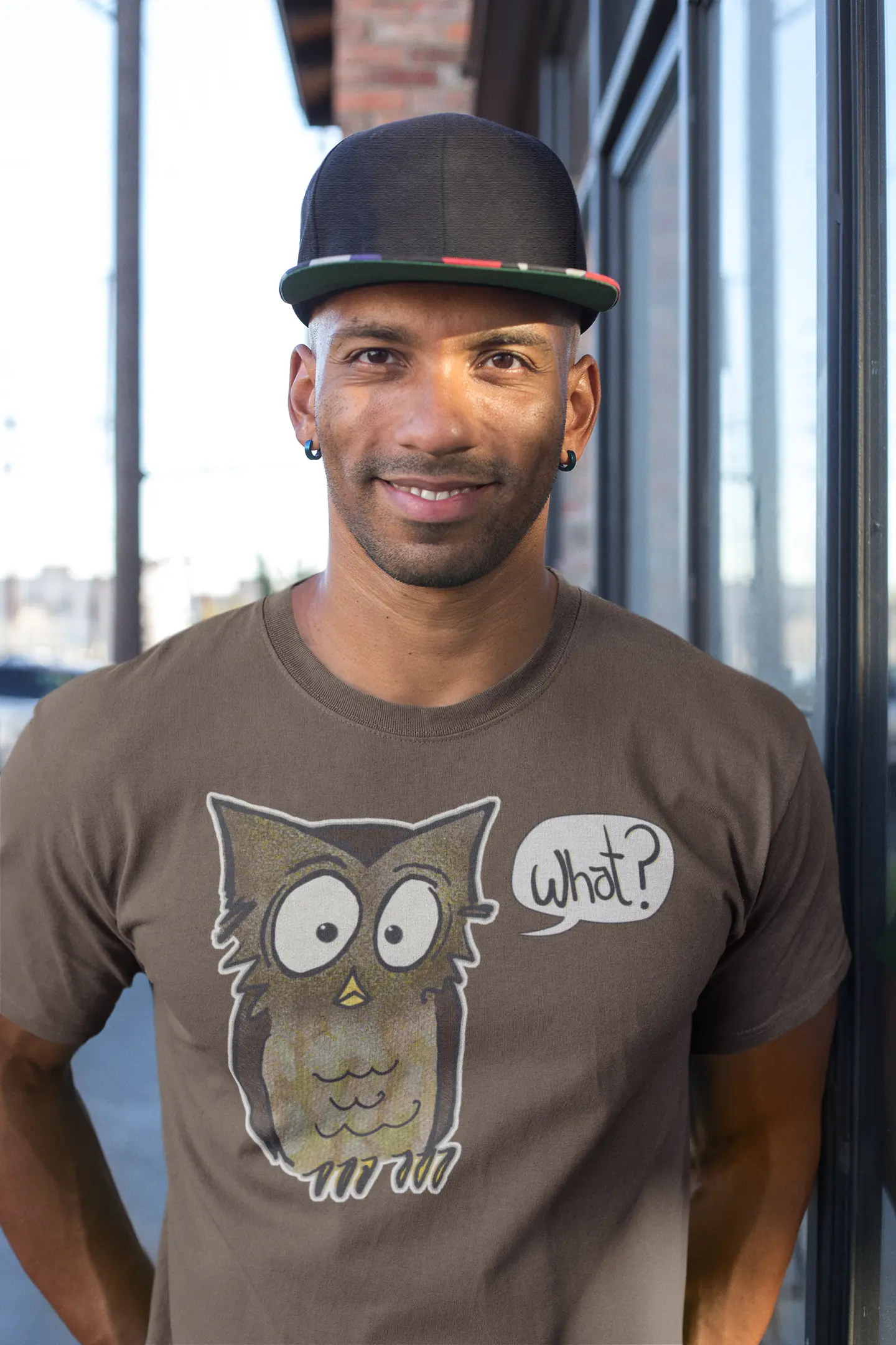 Man wearing a brown t-shirt with an owl graphic and text, standing outdoors.