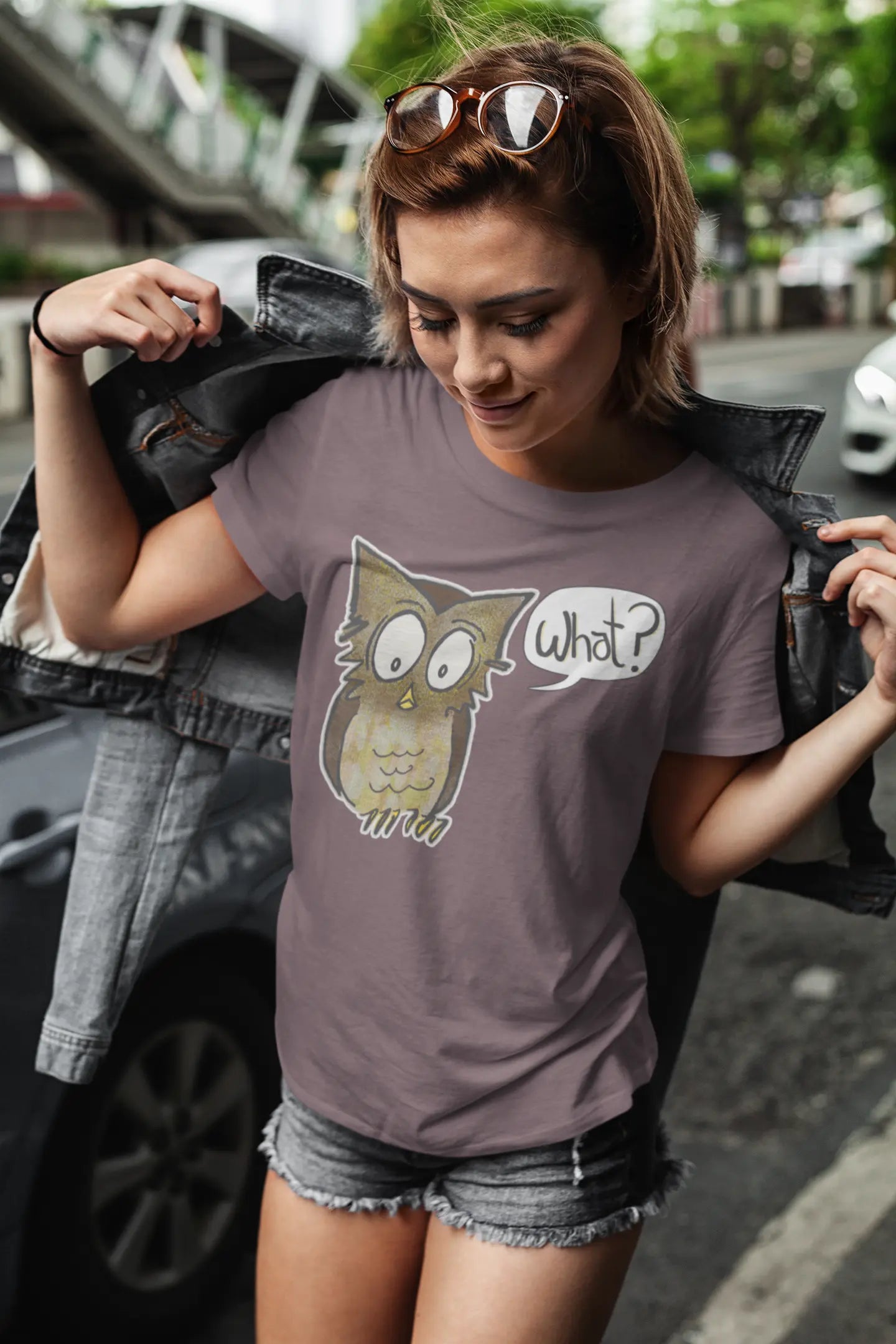 Woman wearing a t-shirt with an owl graphic and text, standing outdoors.