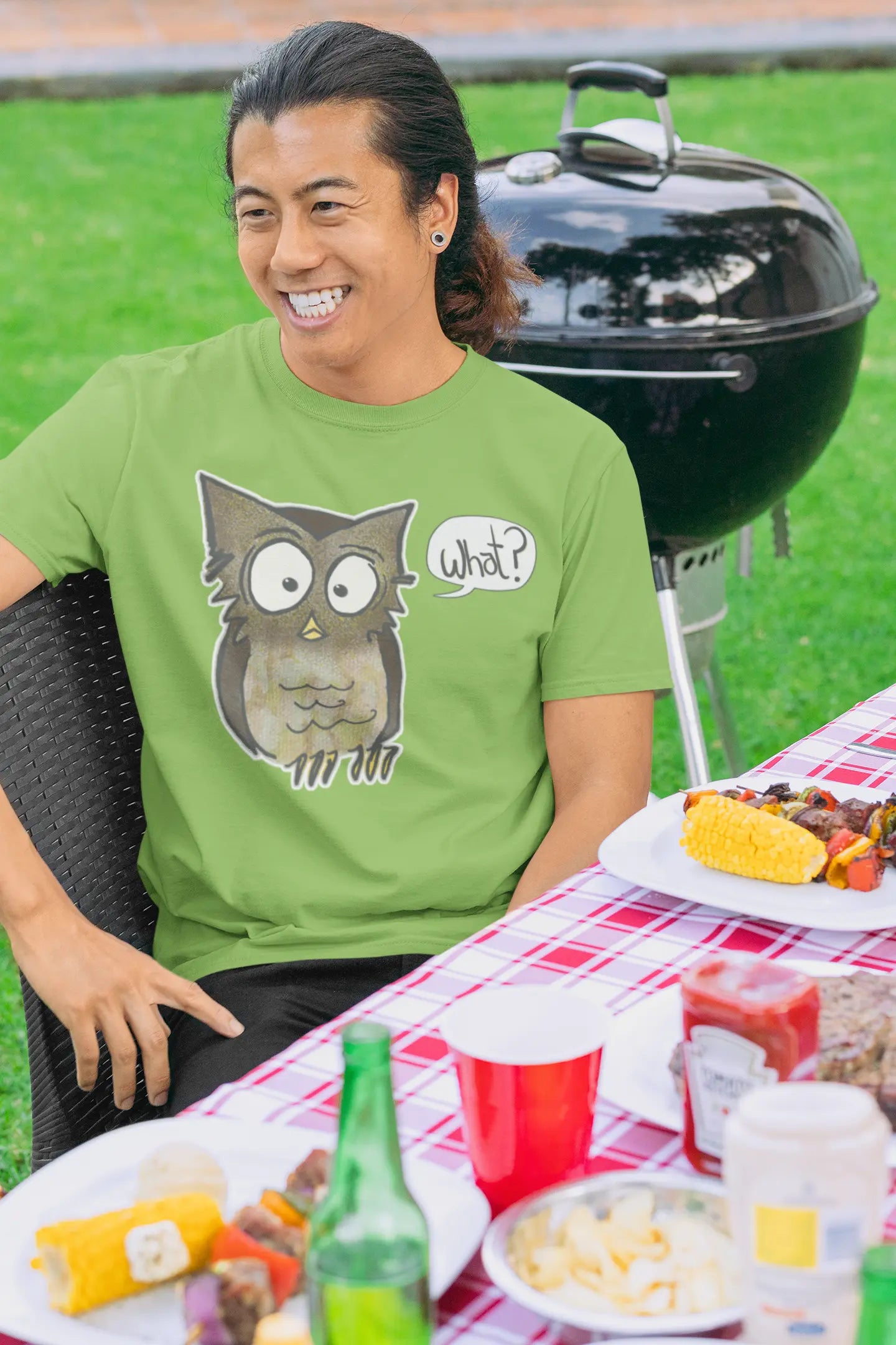 Person wearing a green t-shirt with an owl graphic at a picnic table with food and drinks.