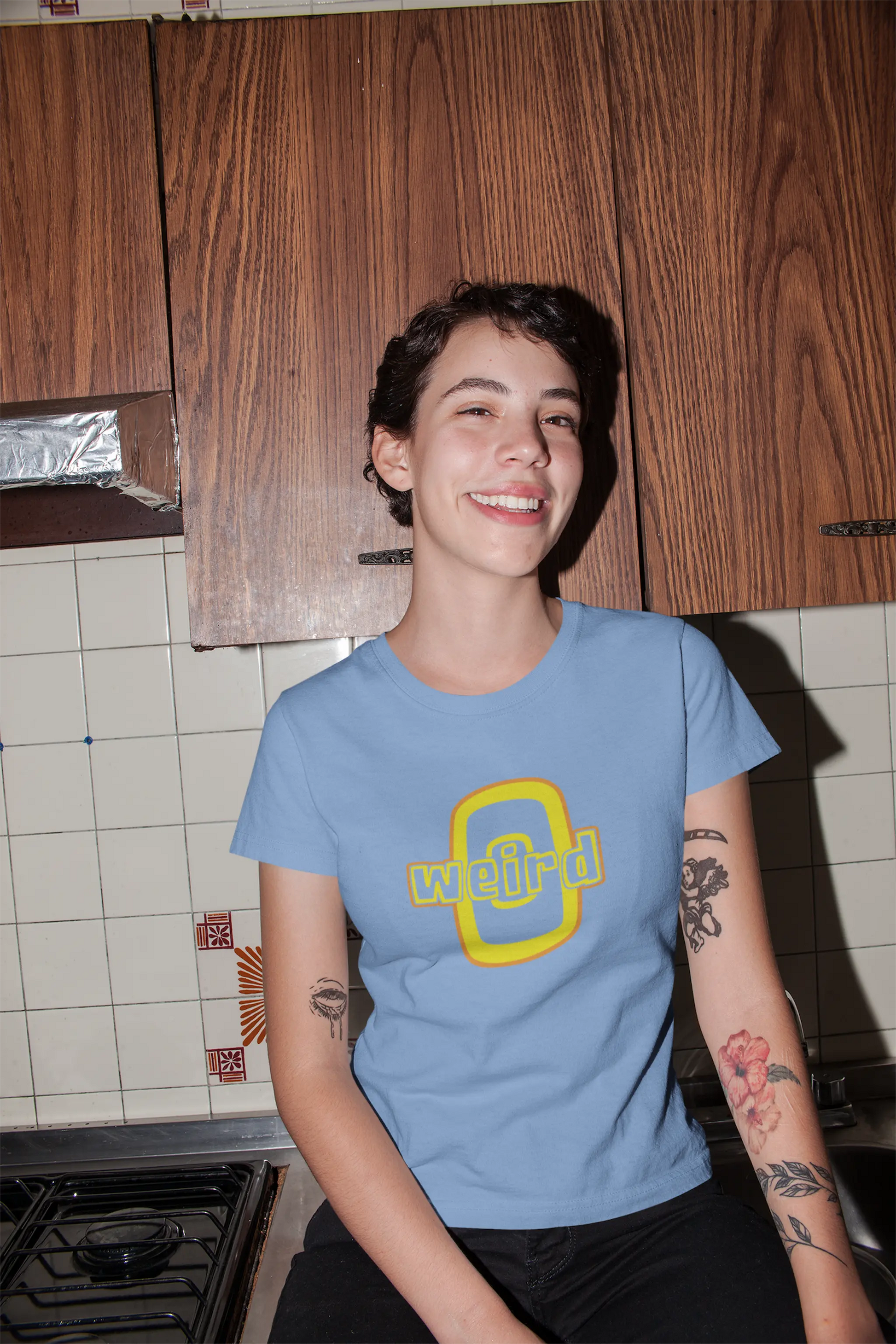 Person wearing a blue Think a Thunk Unisex “Weird” Retro Graphic Tee in a kitchen