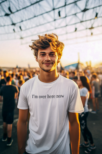 Man wearing a white t-shirt with 'I'm over here now' text in a crowd at sunset.
