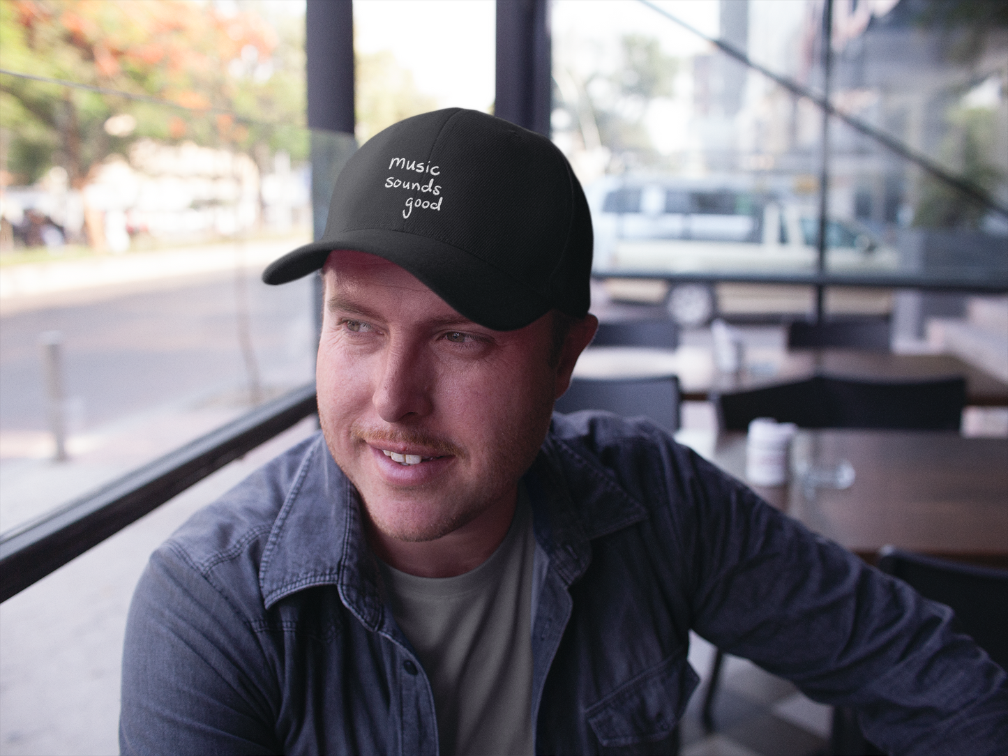Man wearing a black cap with 'music souunds good' text, sitting in a modern indoor setting.