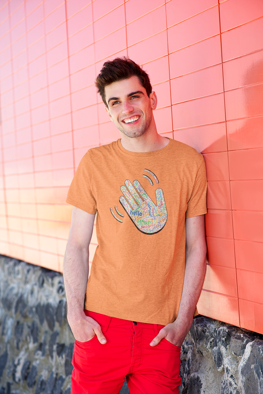 Man wearing an orange T-shirt with a colorful hand graphic filled with greetings from many languages, standing against a pink tiled wall.