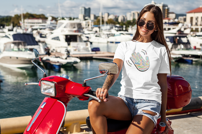 Woman wearing white T-shirt with a colorful hand graphic filled with greetings from many languages, sitting on a red scooter by a marina with boats and buildings in the background