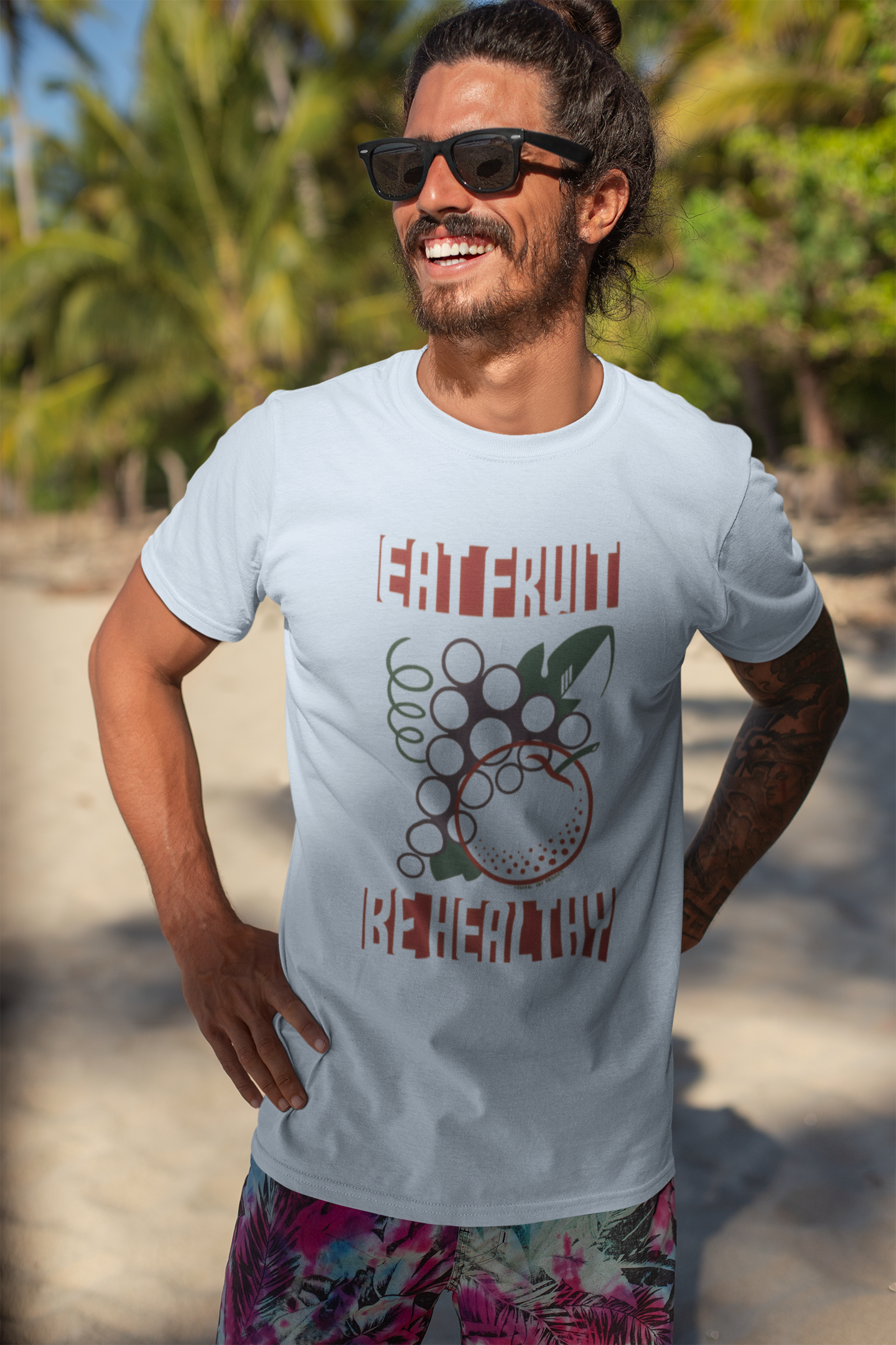 Man wearing a light blue t-shirt with a graphic design and the text "EAT FRUIT BE HEALTHY", standing on a beach.