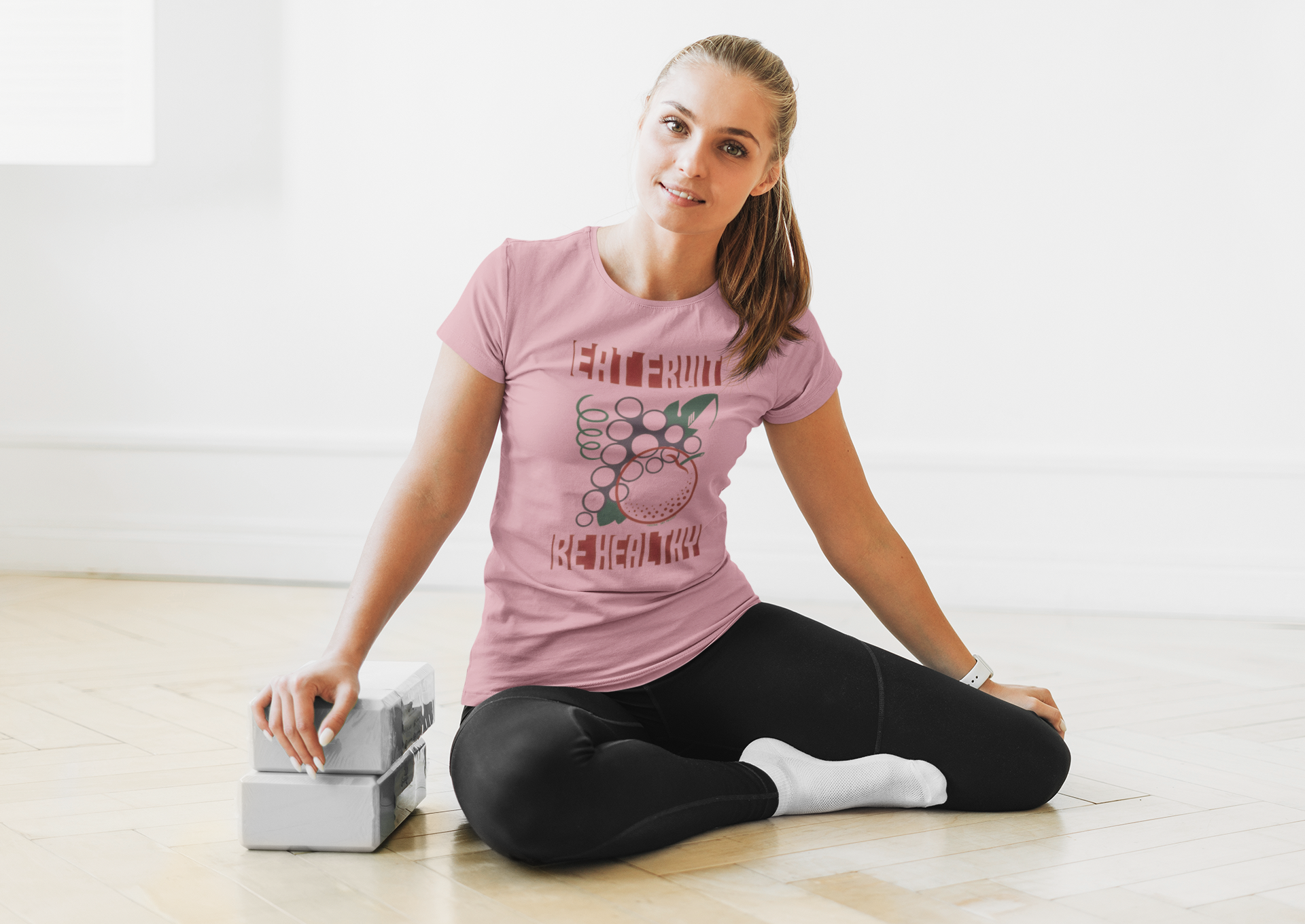 Woman sitting on the floor with a box, wearing a pink t-shirt and black leggings.
